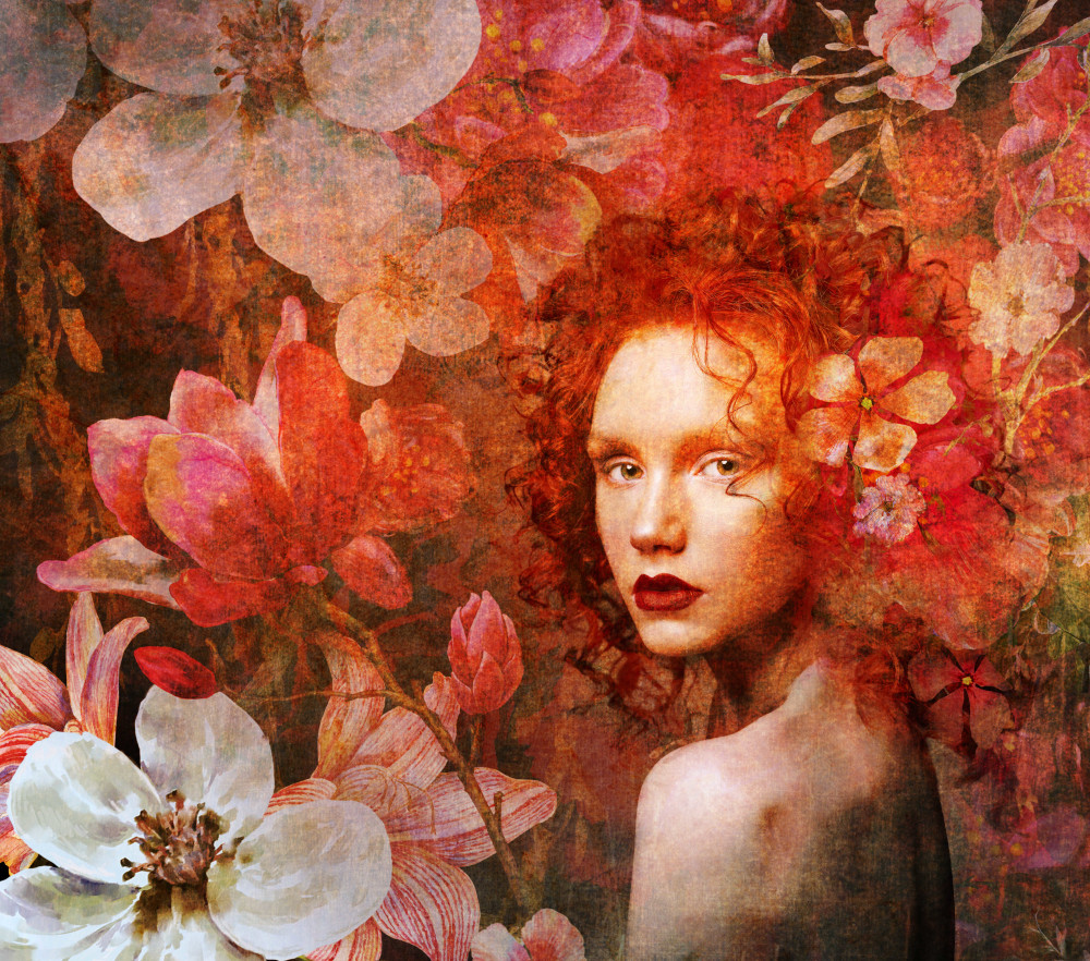 A woman with striking red hair, embellished with flowers, radiating joy in a lush outdoor environment.